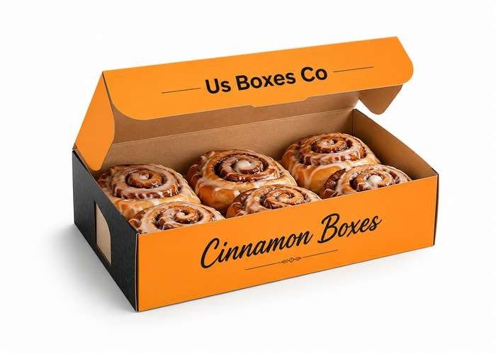 Open orange bakery box filled with iced cinnamon rolls labeled “Cinnamon Boxes” and “Us Boxes Co”.